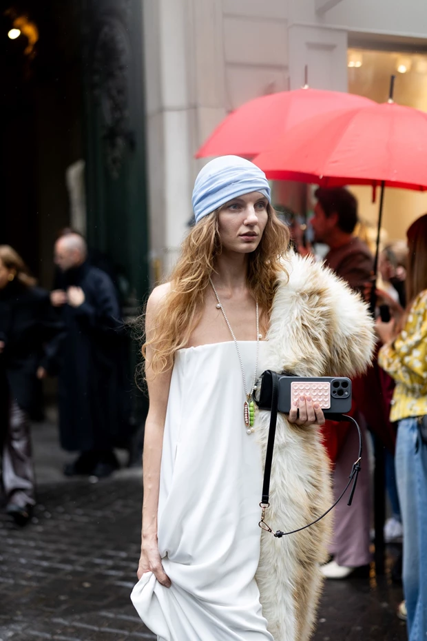 Statement look με μακρύ λευκό στράπλες φόρεμα, ογκώδη γούνα σε μπεζ-καφέ ριγμένη στον ώμο, και γαλάζιο σκούφο/μπαντάνα.