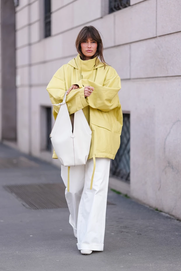 Γυναίκα με λευκό wide leg παντελόνι και oversized κίτρινο jacket σε street style εμφάνιση.