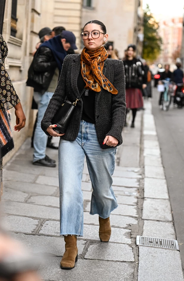 Γυναίκα με τζιν, μπλέιζερ και καφέ σουέτ μποτάκια περπατά στο δρόμο.