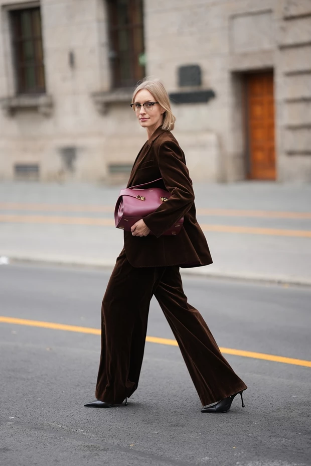 Γυναικείο βελούδινο κοστούμι σε καφέ σοκολατί χρώμα με μπορντό τσάντα, κομψό office look για τις γιορτές 2025.