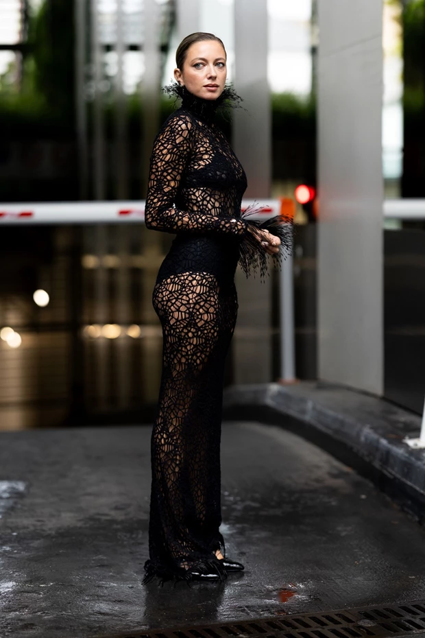 Γυναίκα με μακρύ μαύρο διάφανο φόρεμα από κροσέ με ψηλό γιακά και διακοσμητικά φτερά.