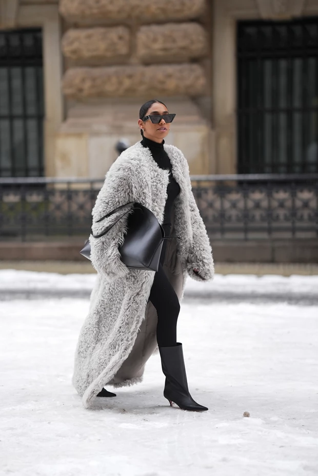 Γυναίκα περπατά στο χιόνι και φοράει γούνινο παλτό, ζιβάγκο και κολάν και μπότες με kitten heel.