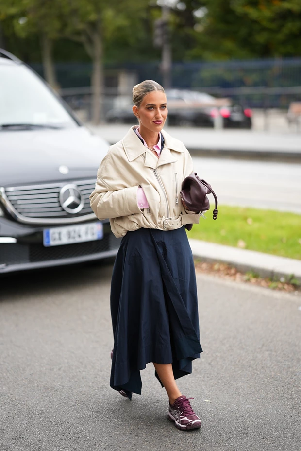 Γυναίκα με μπεζ δερμάτινο jacket, navy μάξι φούστα και μπορντό sneakers, σε κομψό φθινοπωρινό street style σύνολο.