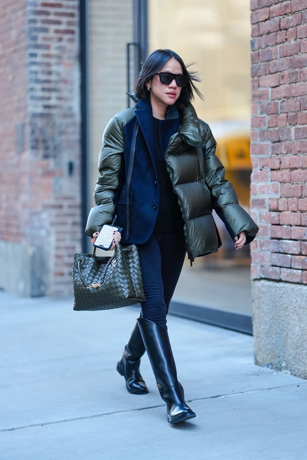 Street style εμφάνιση που συνδυάζει ένα φουσκωτό πράσινο puffer jacket πάνω από ένα αυστηρό ναυτικό μπλε σακάκι και μαύρο παντελόνι.