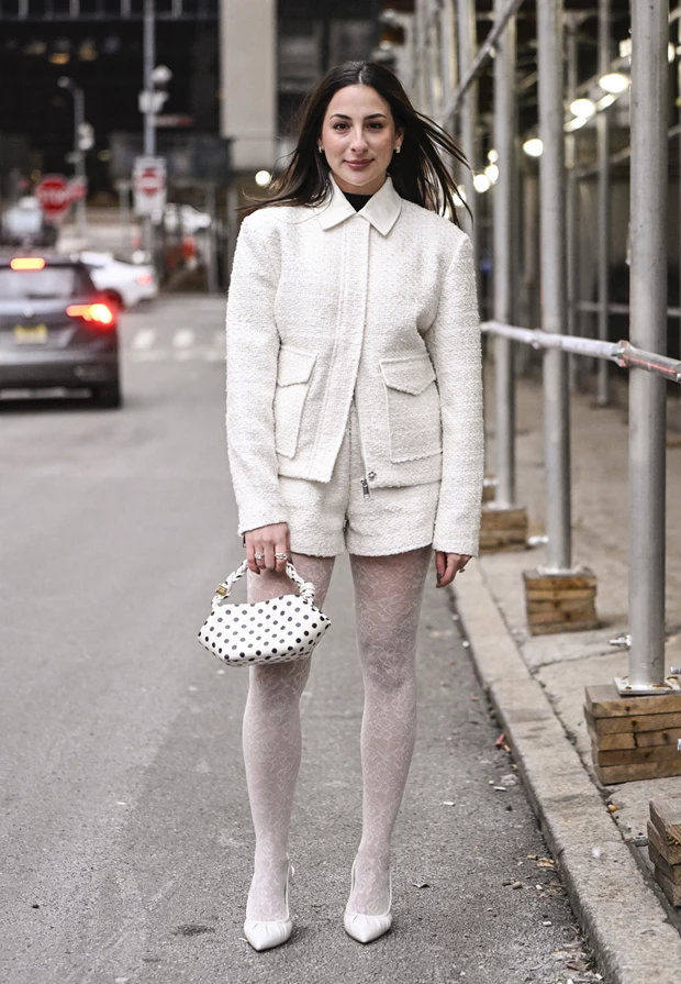 Γυναίκα με total white outfit και λευκές γόβες σε street style εμφάνιση στη Νέα Υόρκη, με σακάκι και σορτς σε tweed ύφος και δαντελένιο καλσόν