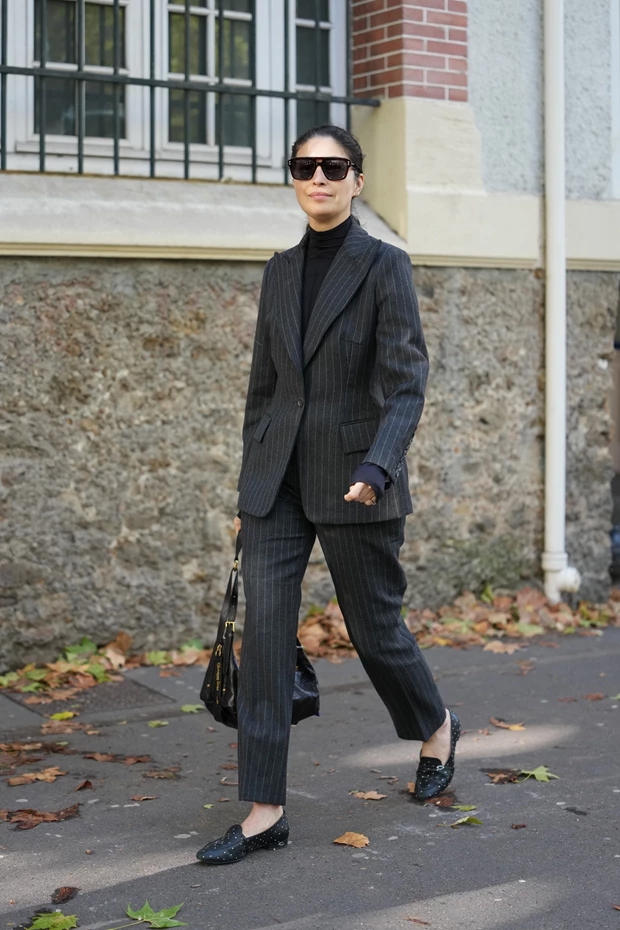 Γυναίκα στον δρόμο με office look. Φοράει γκρι κοστούμι ριγέ, μαύρο ζιβάγκο και μοκασίνια.