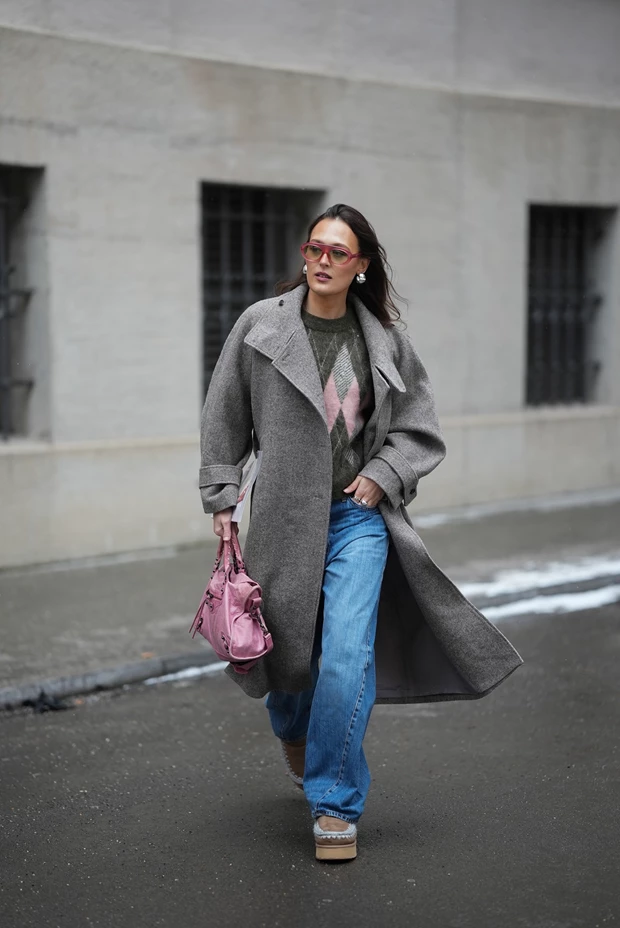 Χειμερινές εκπτώσεις 2026: Γυναίκα στον δρόμο που φοράει γκρι παλτό, argyle πουλόβερ, τζιν και γούνινα μποτάκια.