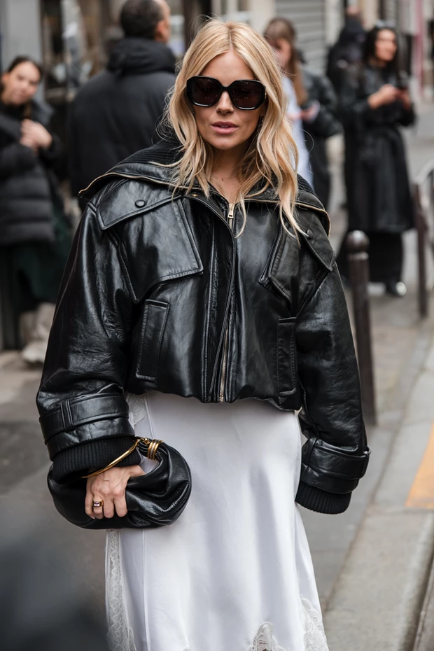 Sienna Miller: Street style look με μαύρο cropped δερμάτινο μπουφάν και λευκή slip φούστα.