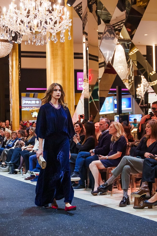 Μοντέλο με μακρύ βελούδινο μπλε σκούρο σύνολο με κόκκινα παπούτσια στην πασαρέλα, Stay Golden Fashion Show Golden Hall.