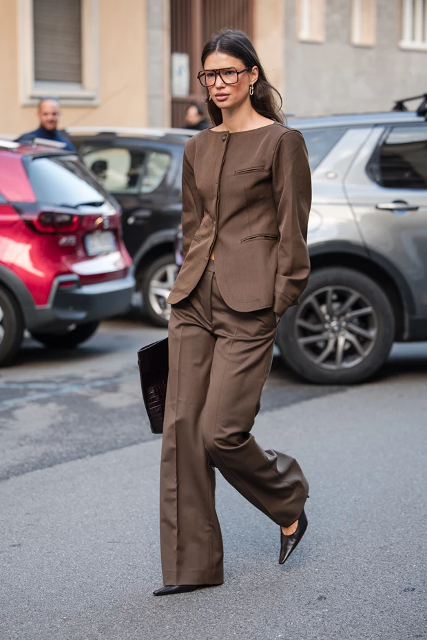 Γυναίκα στον δρόμο με καφέ tailored κοστούμι, μυτερές γόβες και γυαλιά μυωπίας.