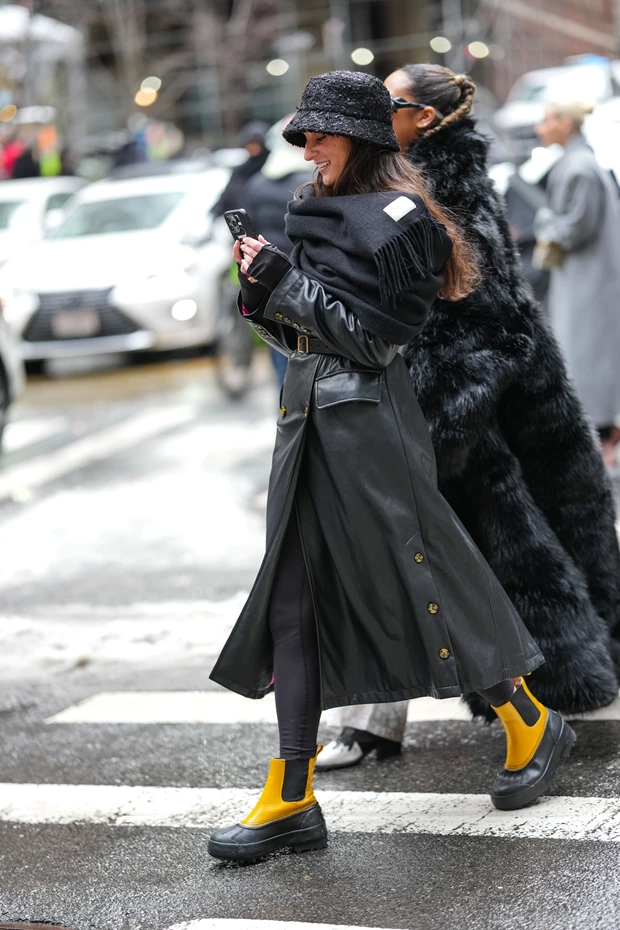 Γυναίκα στο κρύο φοράει καμπαρντίνα δερμάτινη, κασκόλ και μπότες γαλότσες.