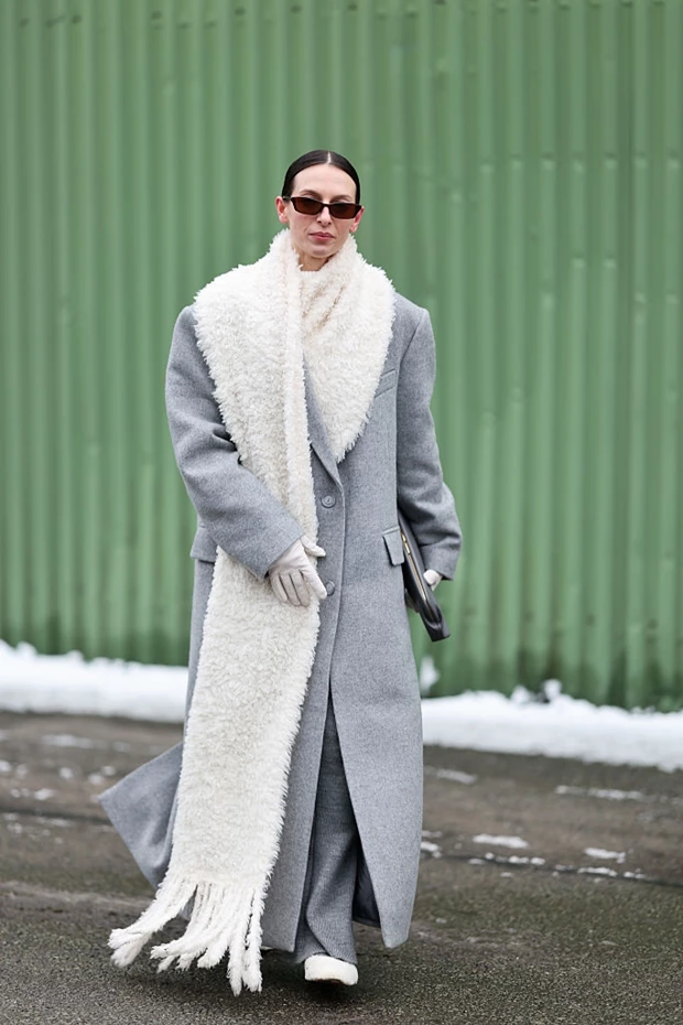 Minimal χειμερινό look με μακρύ γκρι παλτό και oversized λευκό κασκόλ σε street style εμφάνιση Σκανδιναβίδας