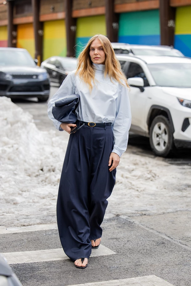 Γυναίκα με ψηλόμεσο navy wide leg παντελόνι και γαλάζια μπλούζα tucked-in, με μαύρα flat sandals.