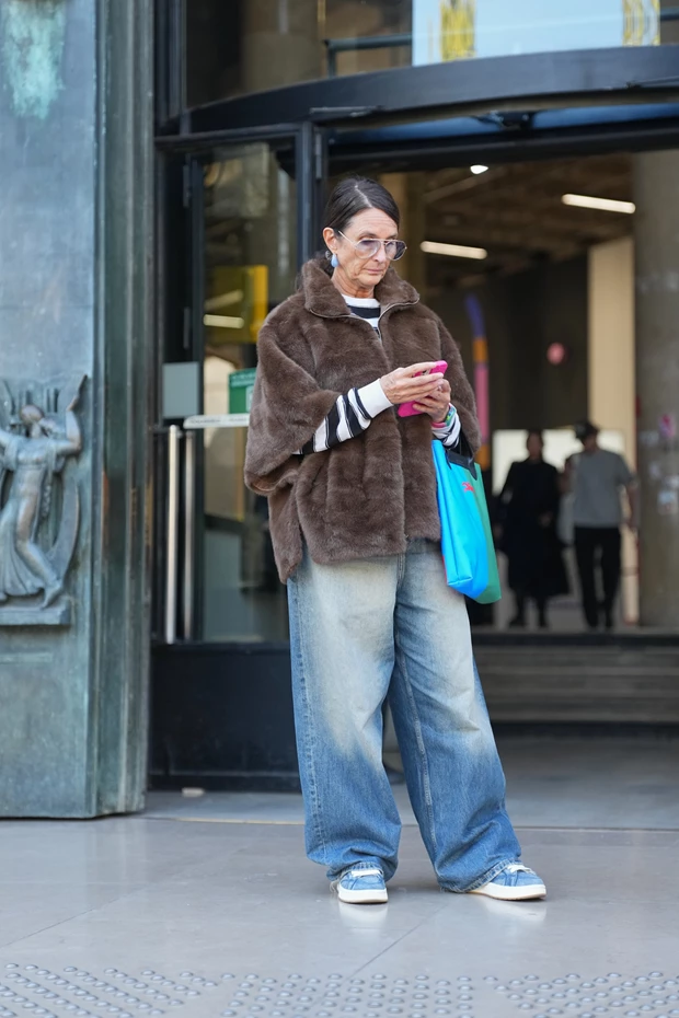 Γυναίκα έχει συνδυάζει καφέ κοντό τζάκετ από γούνα με φαρδύ τζιν παντελόνι και sneakers.