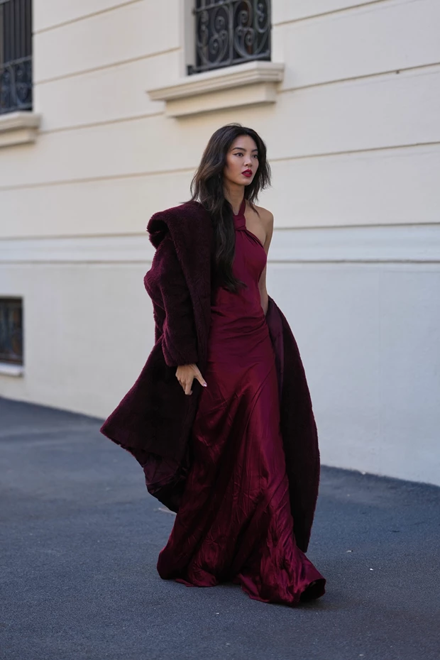 Γυναίκα με μακρύ βουργουνδί σατέν φόρεμα και ασορτί ψεύτικη γούνα σε δρόμο της πόλης.