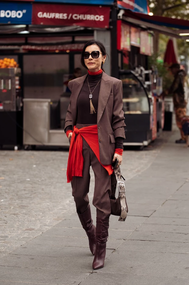 Σκούρο καφέ κοστούμι με κόκκινο πουλόβερ δεμένο στη μέση και μακριές κόκκινες μπότες.
