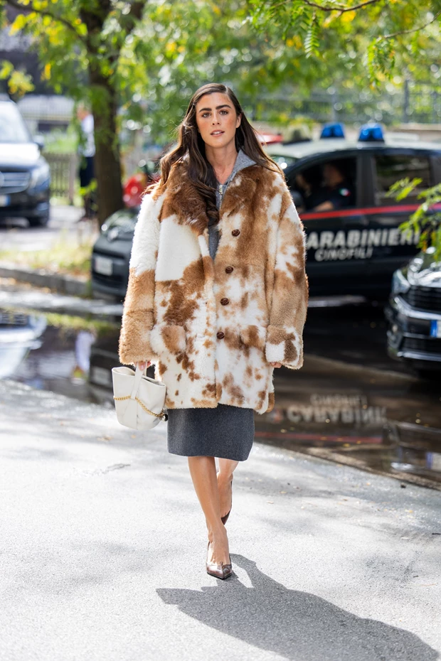 Κομψή εμφάνιση street style με κοντή γκρι φούστα, ογκώδες παλτό με απομίμηση γούνας animal print, και μια μικρή λευκή τσάντα.