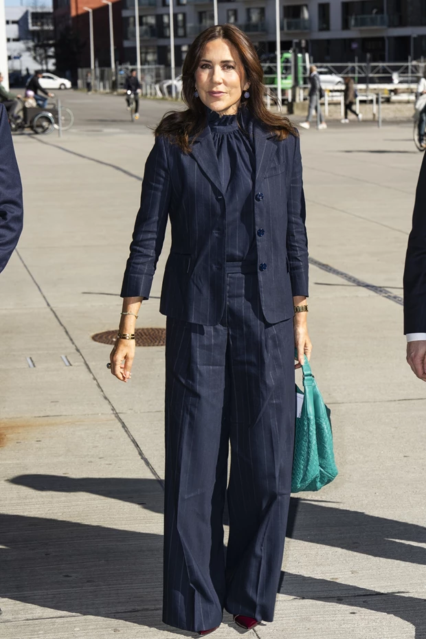 Η Βασίλισσα Mary της Δανίας με navy pinstripe κοστούμι, ψηλόλαιμο τοπ και κρατώντας μια έντονη πράσινη τσάντα.
