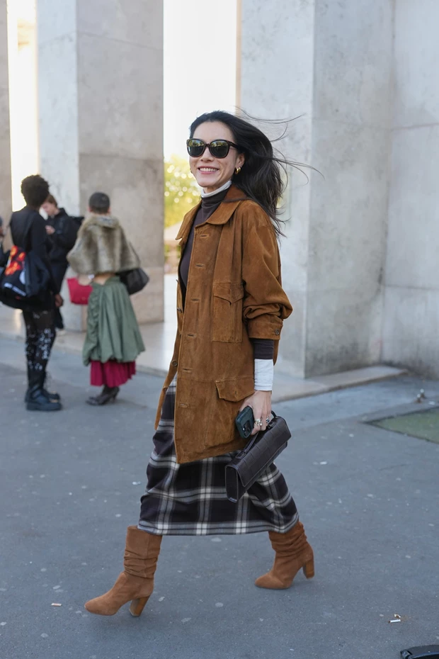 Γυναίκα με καφέ σουέτ σακάκι, καφέ-γκρι καρό φούστα και σουρωτές καφέ μπότες.