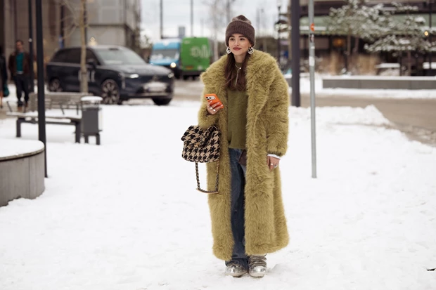 Γυναίκα με μακρύ faux fur παλτό, πλεκτό σκουφί και τζιν σε χειμερινό street style look στην Κοπεγχάγη