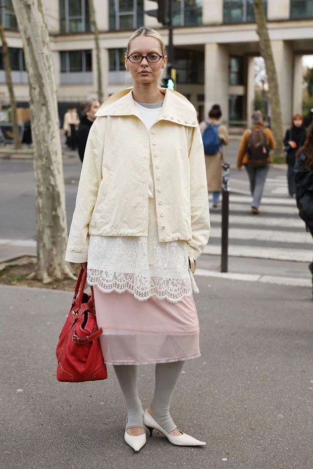 Γυναίκα με λευκό jacket και ροζ παστέλ φούστα, που κρατάει μια έντονη κόκκινη τσάντα ως pop of color στο σύνολο.