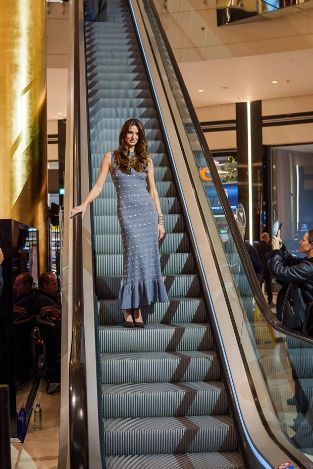 Η Ηλιάνα Παπαγεωργίου με κομψό, εφαρμοστό γκρι φόρεμα με κέντημα και ουρά (ruffle hem), σε μοντέλο στην κυλιόμενη σκάλα του Golden Hall.