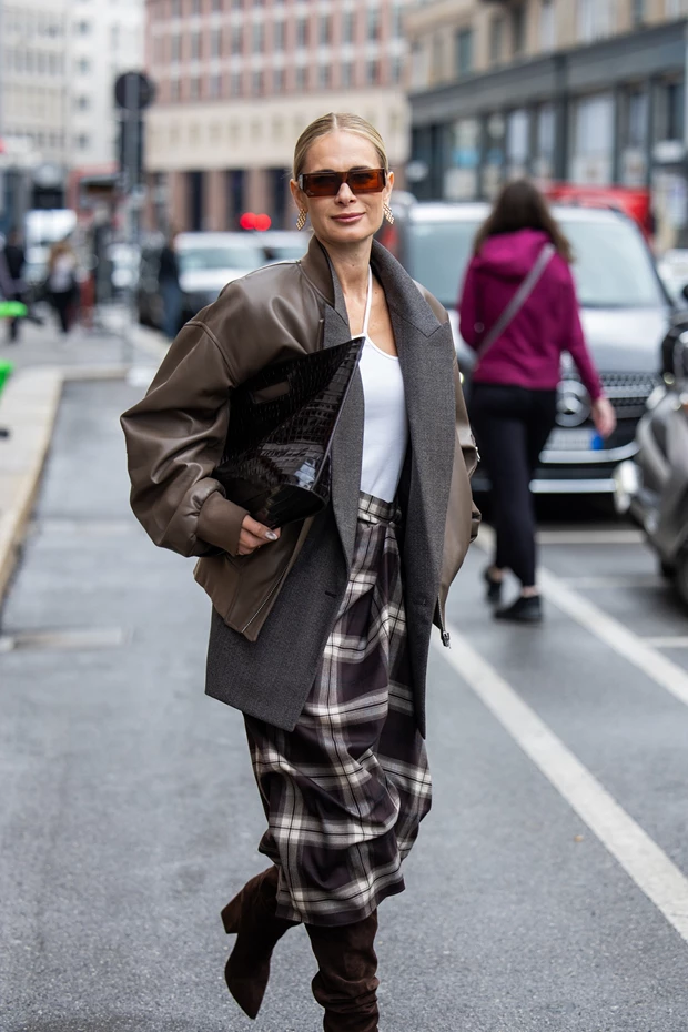 Γυναίκα με καρό μάξι φούστα, δερμάτινο μπουφάν, γκρι σακάκι και ψηλές μπότες, street style.