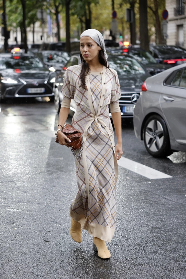 Γυναίκα περπατά στον δρόμο φορώντας μακρυμάνικο μίντι πλεκτό φόρεμα σε μπεζ-καφέ καρό σχέδιο, σουέτ μποτάκια και μαντήλι στο κεφάλι.