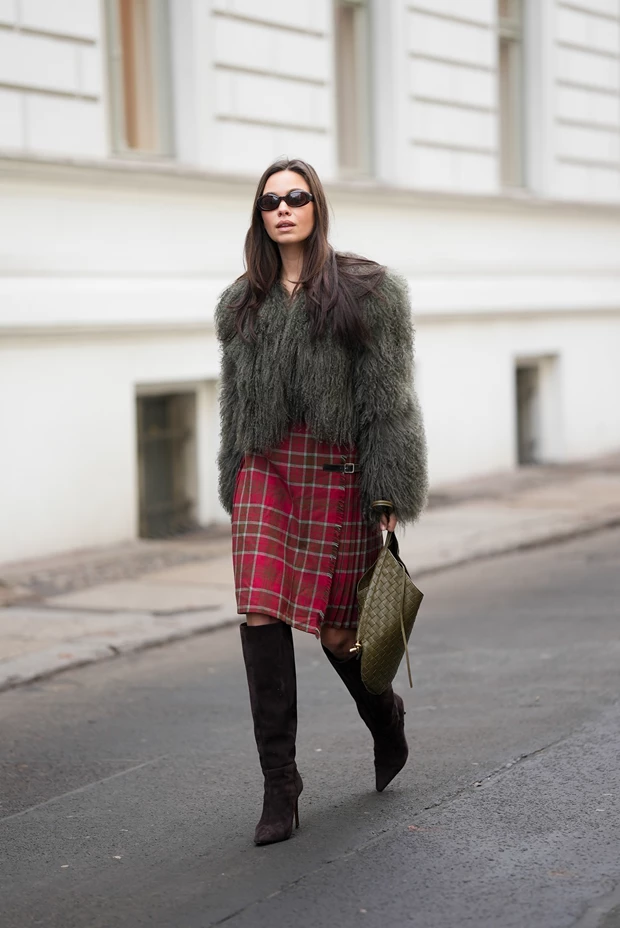 Γιορτινό ντύσιμο γραφείου με κόκκινη καρό φούστα, γούνινο jacket σε χακί χρώμα και καφέ σουέντ μπότες, τάσεις μόδας 2025.