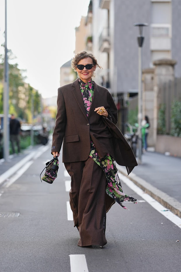 Καφέ, υπερμεγέθες κοστούμι φορεμένο πάνω από ένα μακρύ, floral φόρεμα.