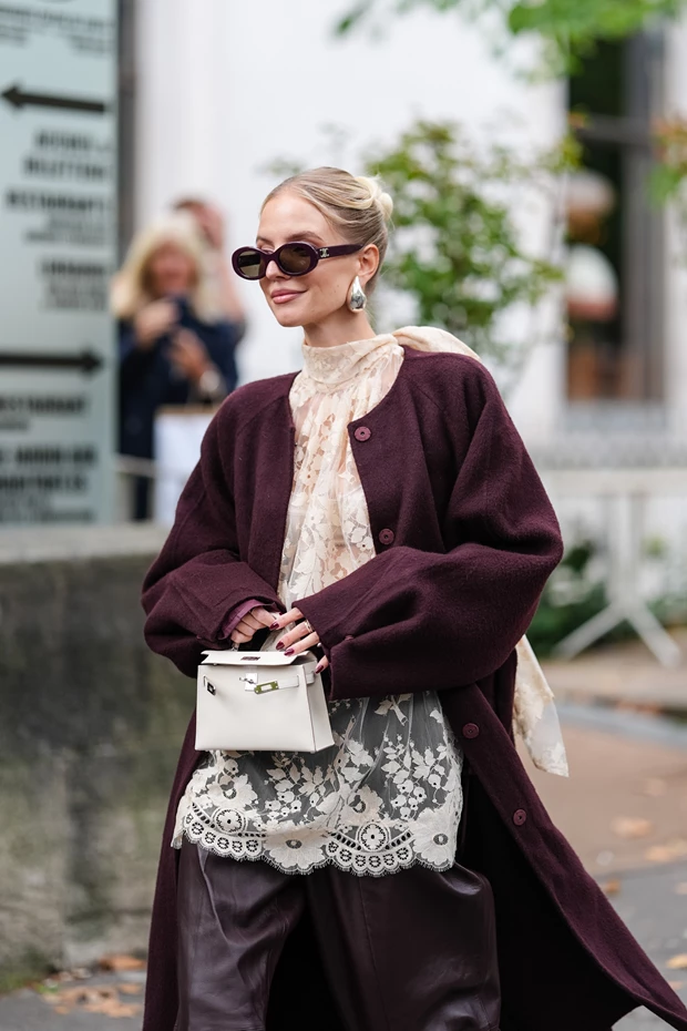 Γυναίκα στο Παρίσι που φοράει μπροντό παλτό με δαντελένια μπλούζα και δερμάτινο παντελόνι. Έχει λευκή μίνι τσάντα και μαύρα γυαλιά ηλίου.